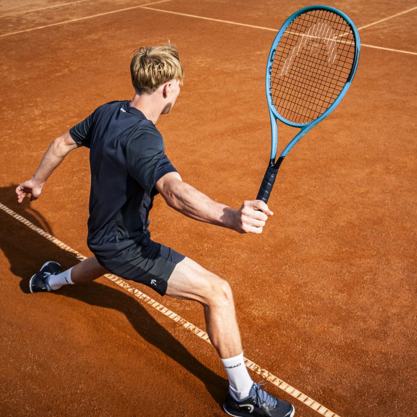 Tennis player in action on a clay court with a blue racket
