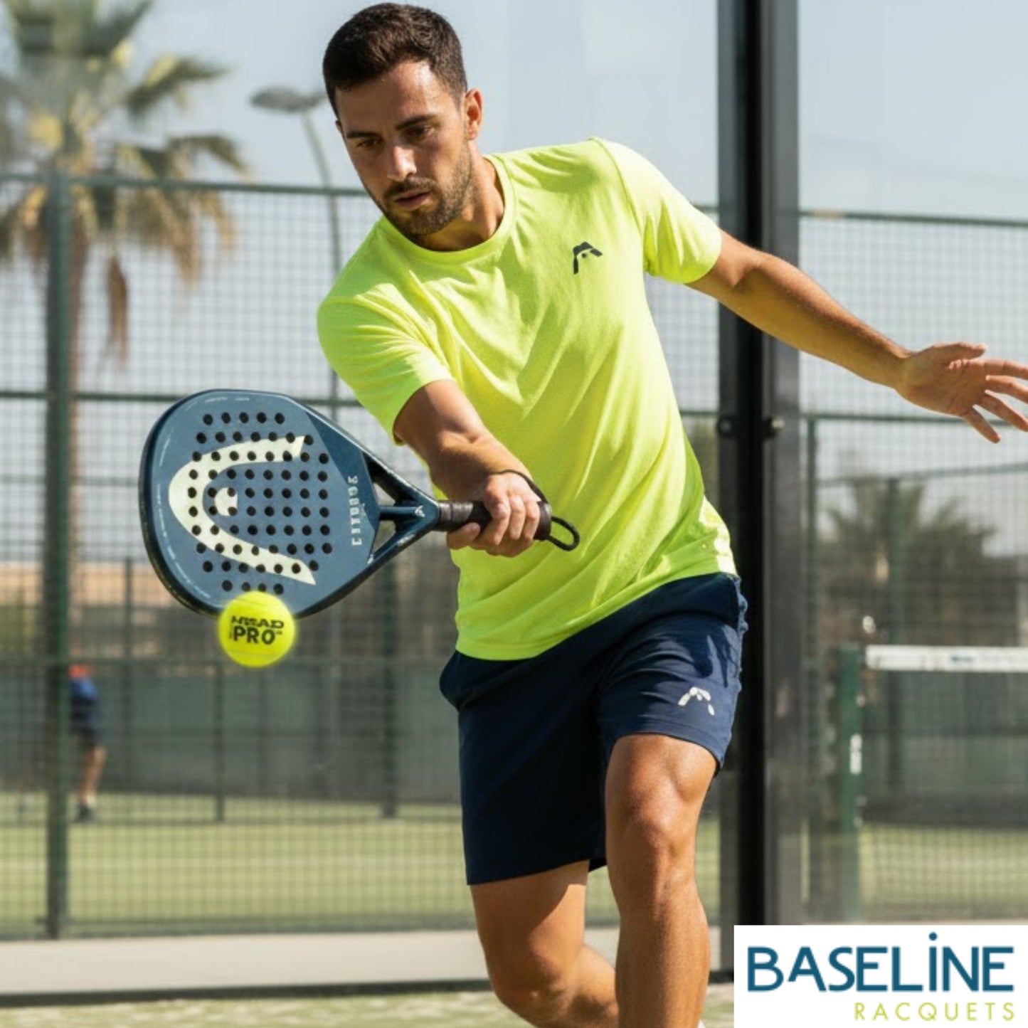 Man playing paddle tennis on a court with 'Baseline Racquets' branding.