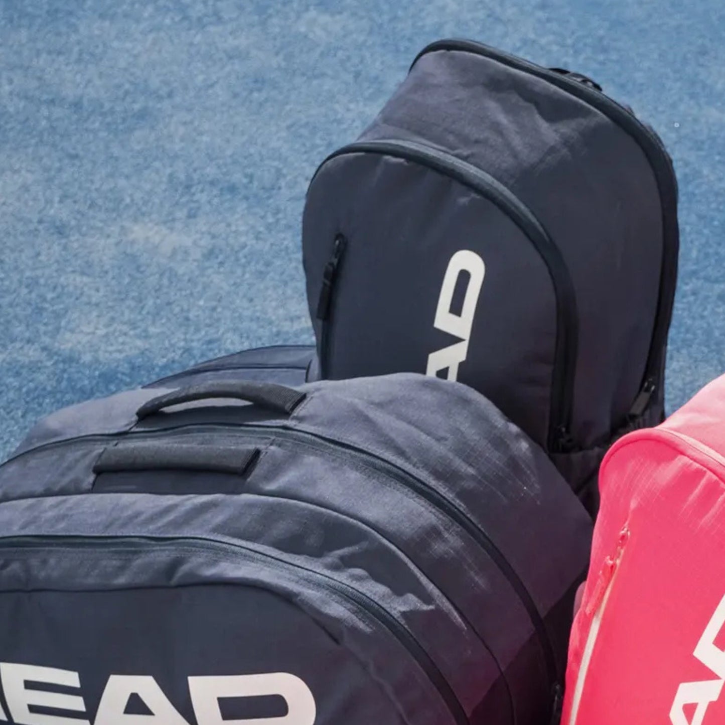 Two tennis bags with 'HEAD' branding on a blue tennis court.