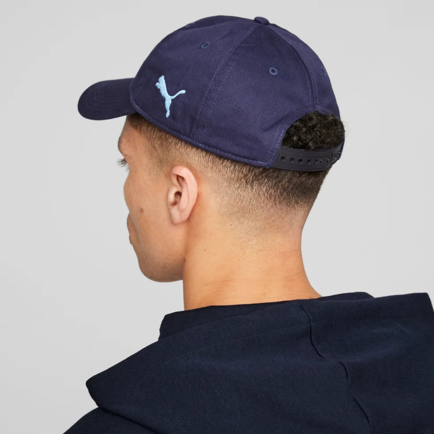Person wearing a navy blue cap with a logo on the back, against a light gray background
