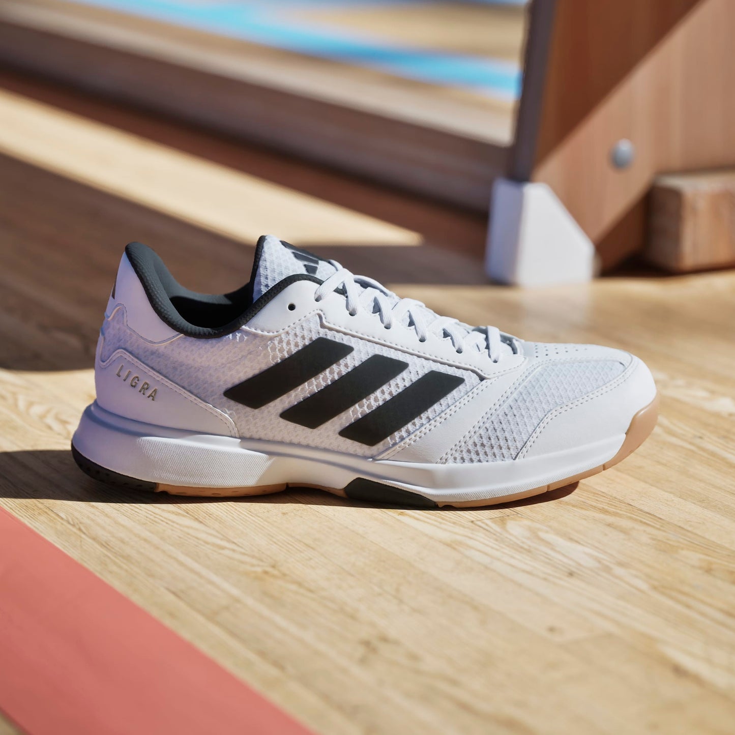 White Adidas squash shoe with black stripes on a wooden floor