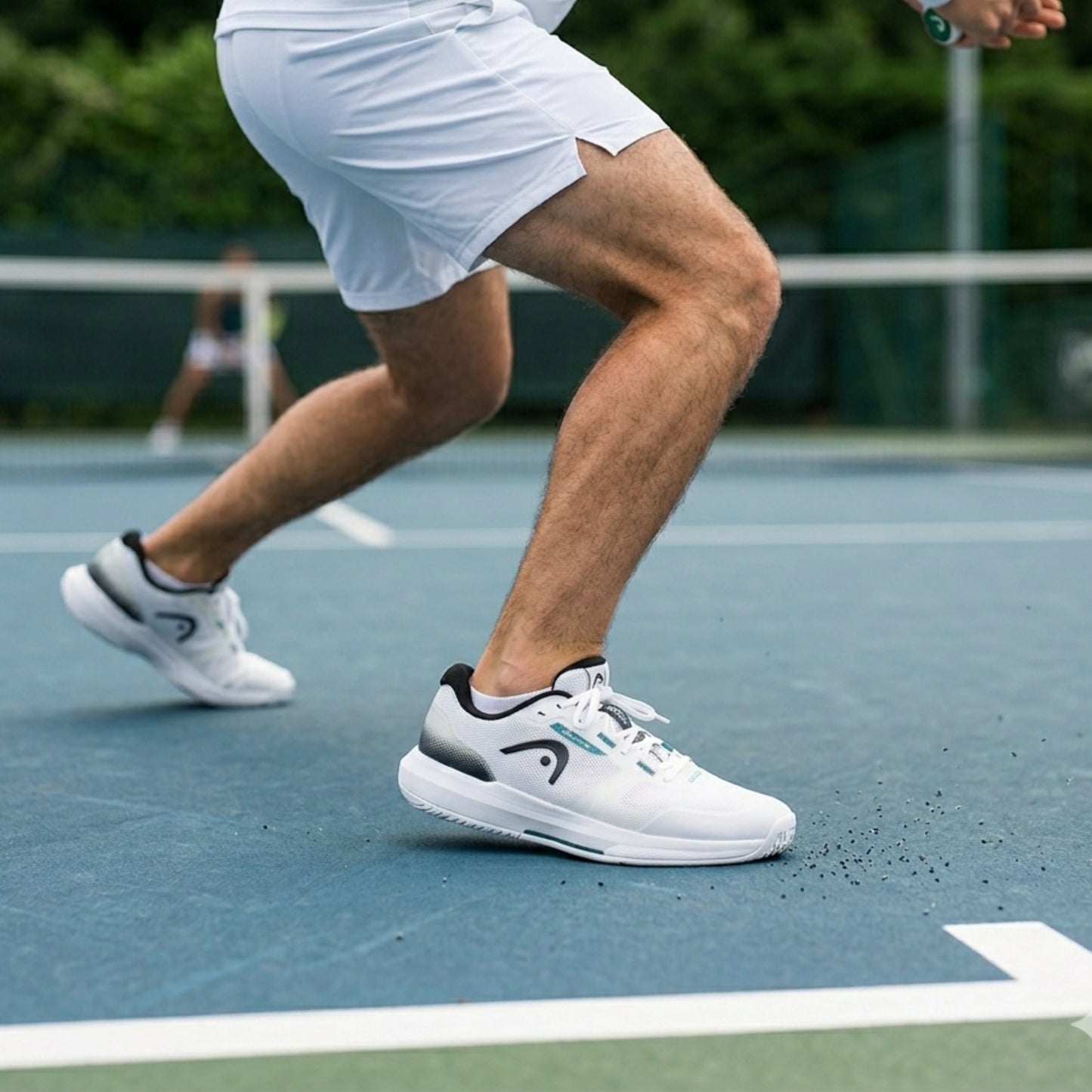 Person playing tennis on a court wearing white shoes with a brand logo.
