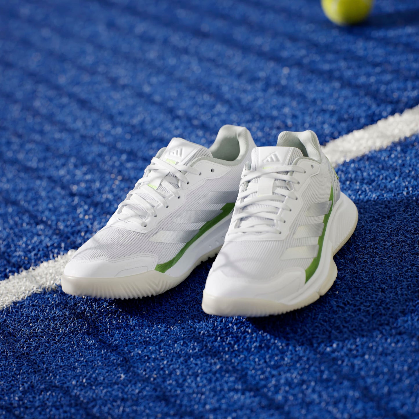 White padel shoes with green accents on a blue tennis court surface.