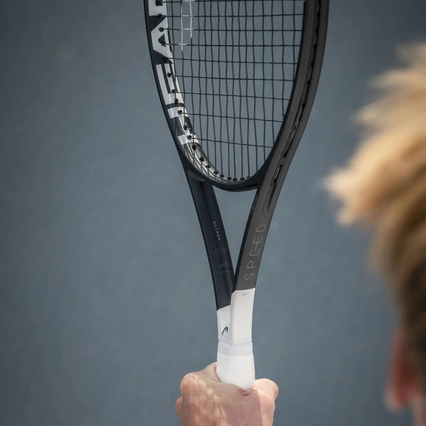 Tennis racket with 'HEAD' branding held by a person against a gray background