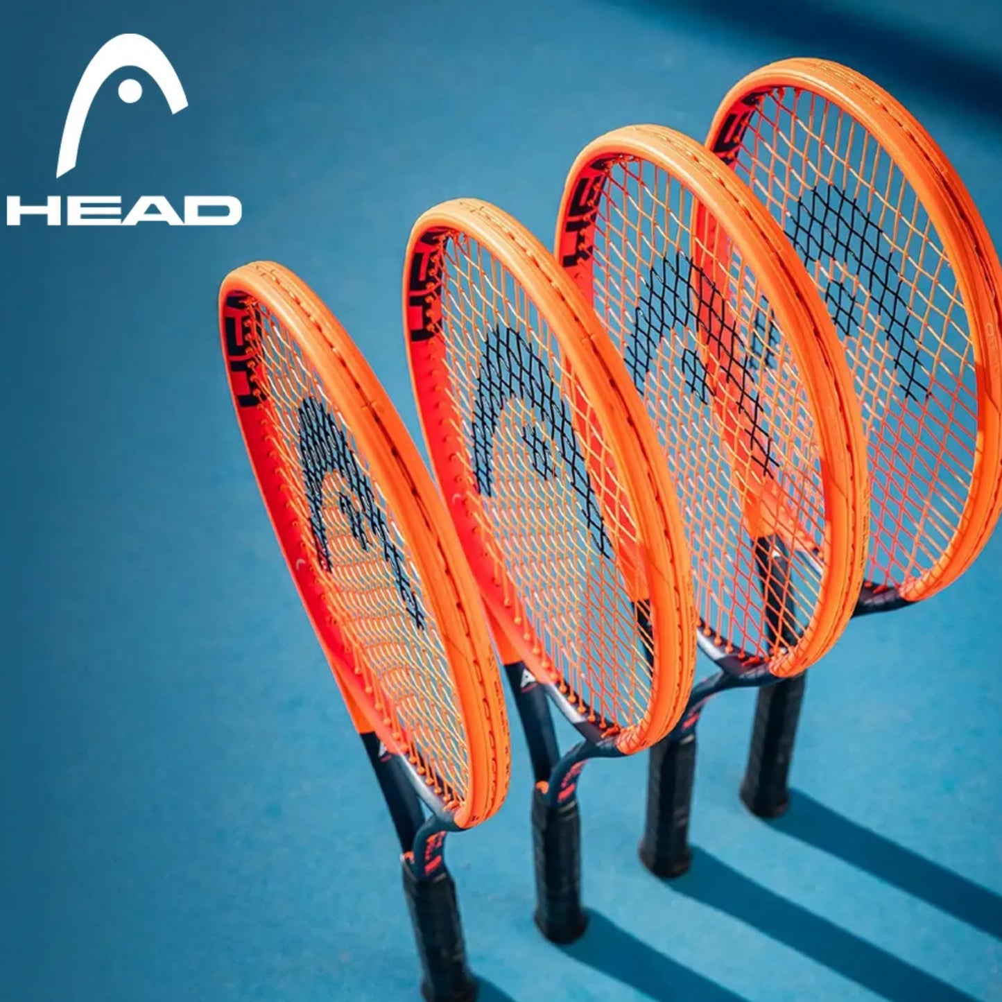 Four Head orange tennis rackets with black strings on a blue background, featuring the HEAD logo.