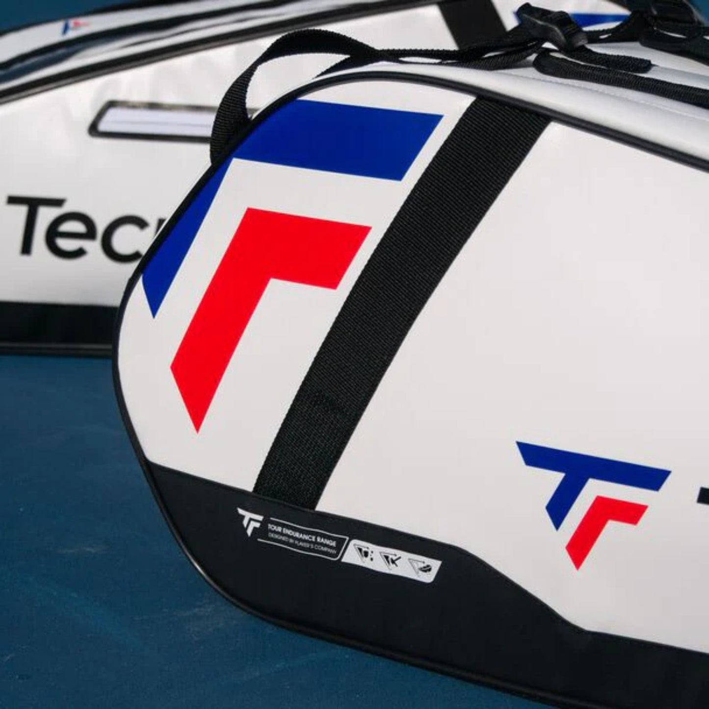 White tennis racket bag with red and blue logo on a blue surface