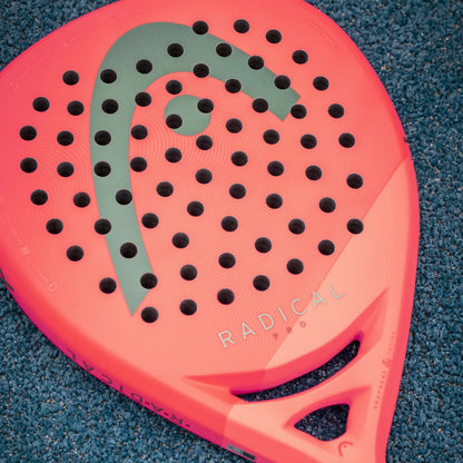 Red Head padel racket with black holes and a green logo on a blue textured surface
