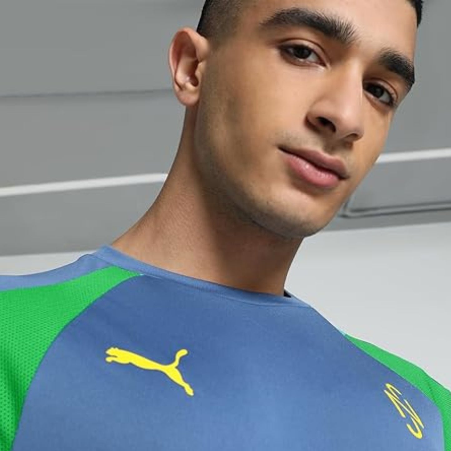 Person wearing a blue and greenPuma soccer jersey with a yellow logo on a neutral background