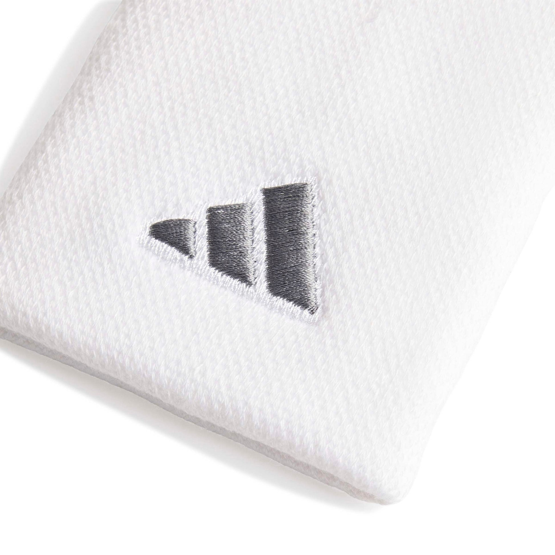 A close-up of a white wristband accessory featuring a dark gray embroidered Adidas logo.