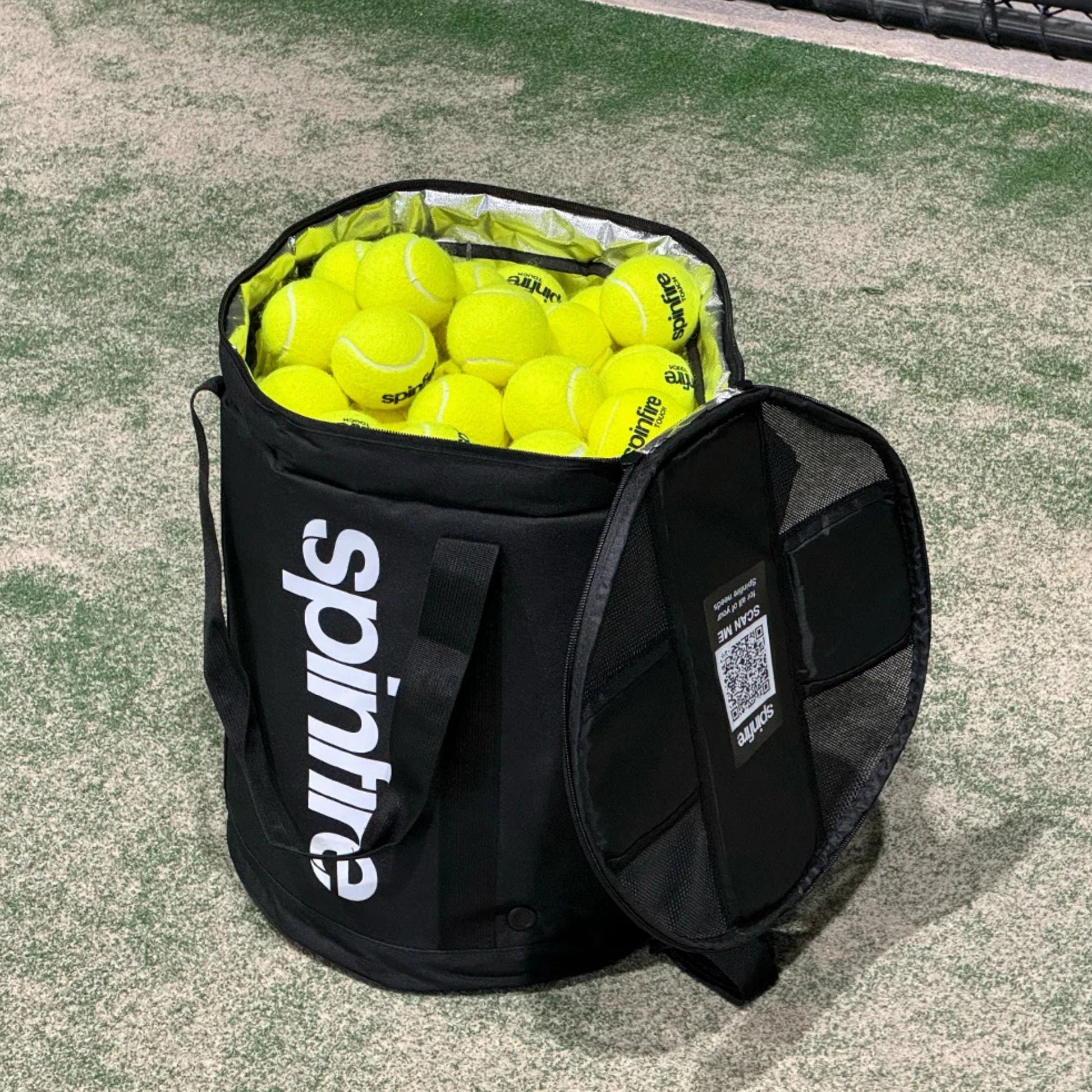 Black Spinfire tennis ball bag filled with yellow balls on a tennis court.