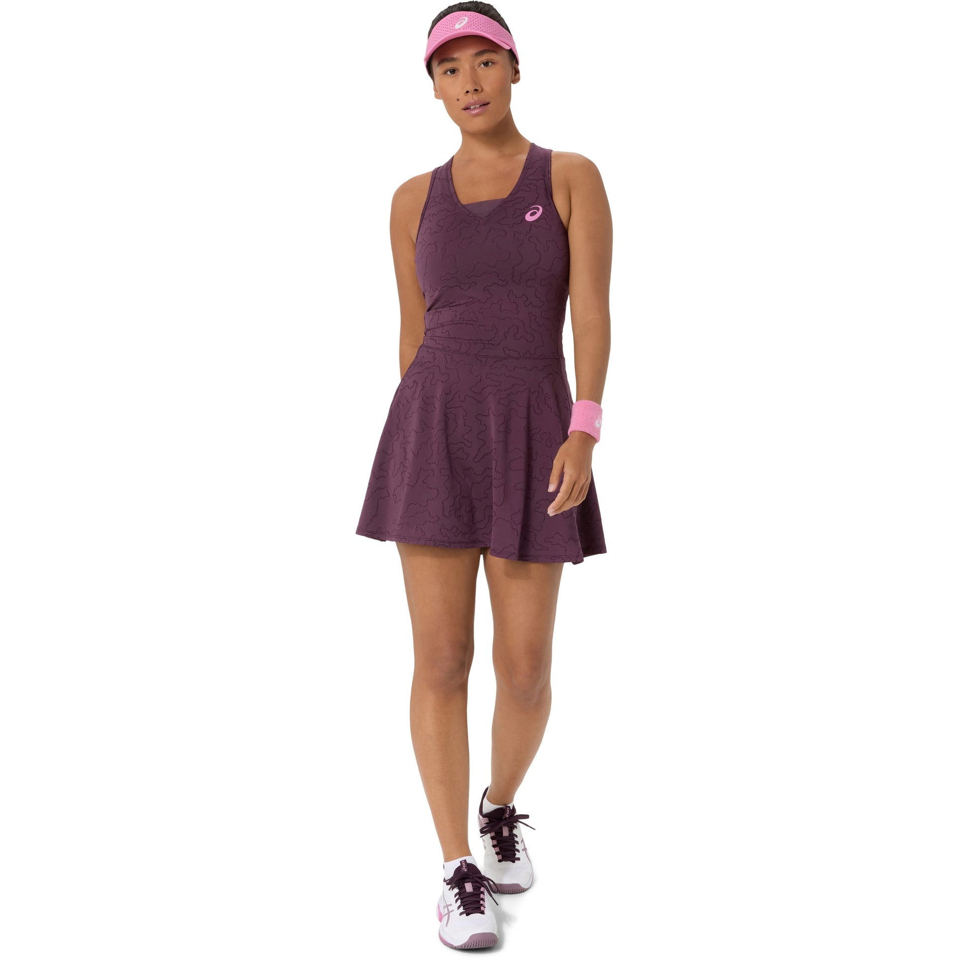 A woman modeling an athletic tennis dress in heathered plum purple, paired with a matching pink visor, wristband, and athletic shoes, against a plain white background.