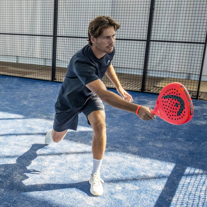 Man playing padel tennis on a blue court with a red paddle.