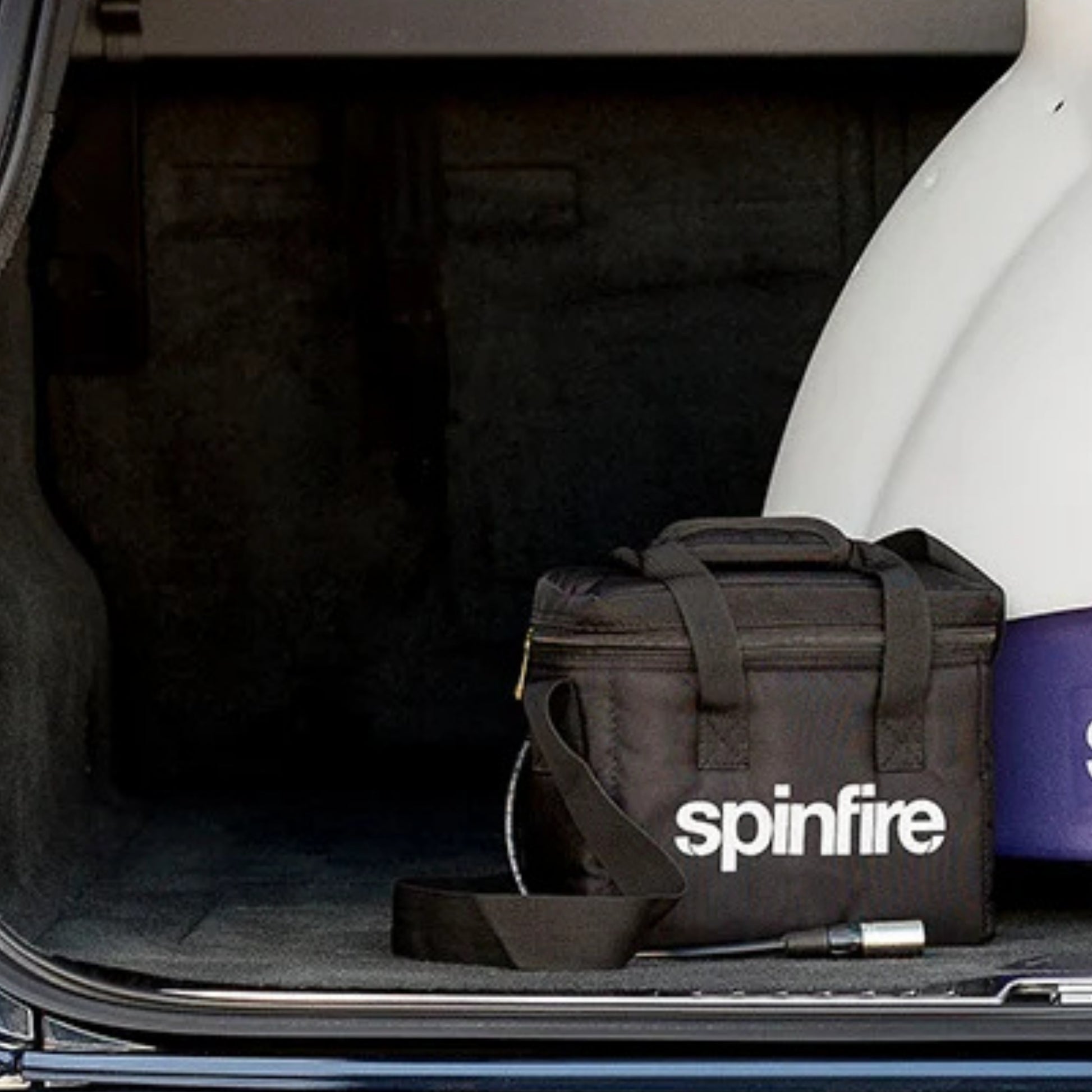Black 'spinfire' bag in a car trunk with a white object next to it.