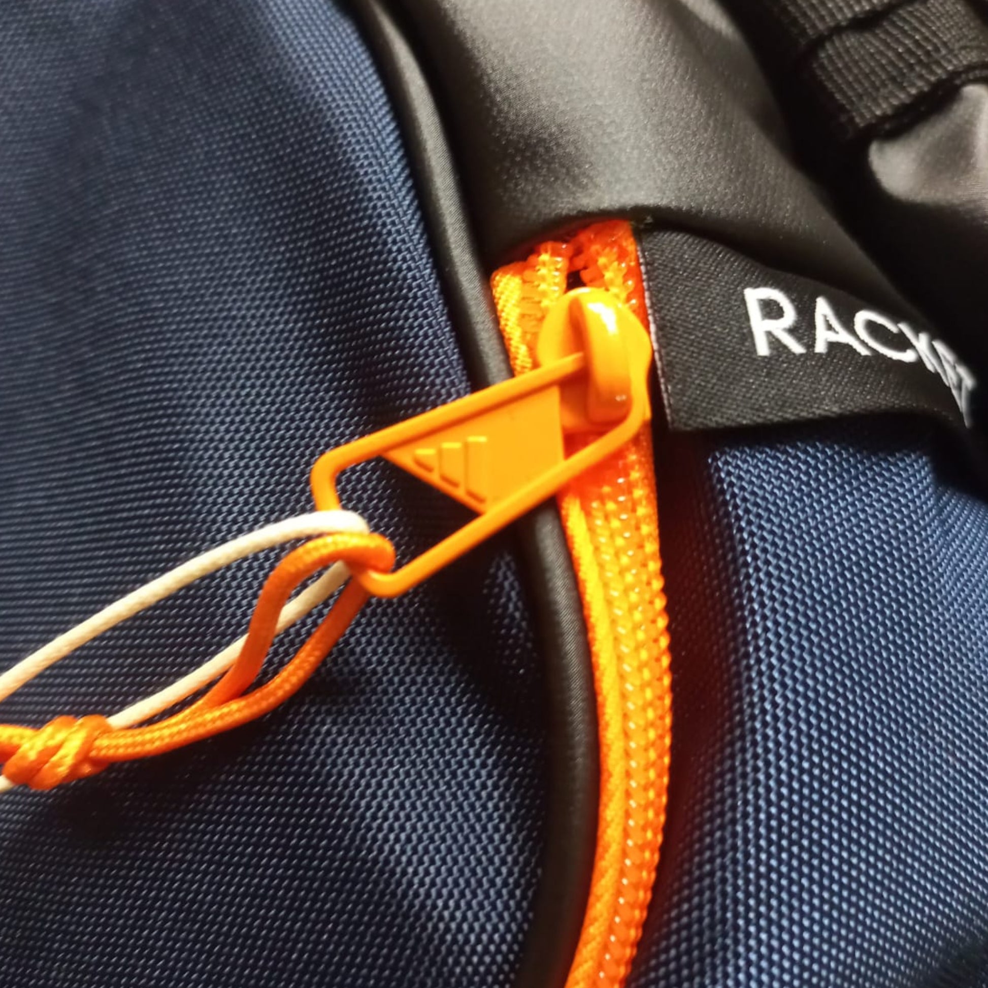 Close-up of a navy blue bag with an orange zipper and 'Racket' branding.
