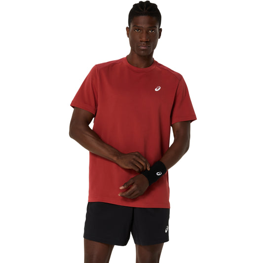 Man wearing a red athletic Asics shirt and black shorts with a white background