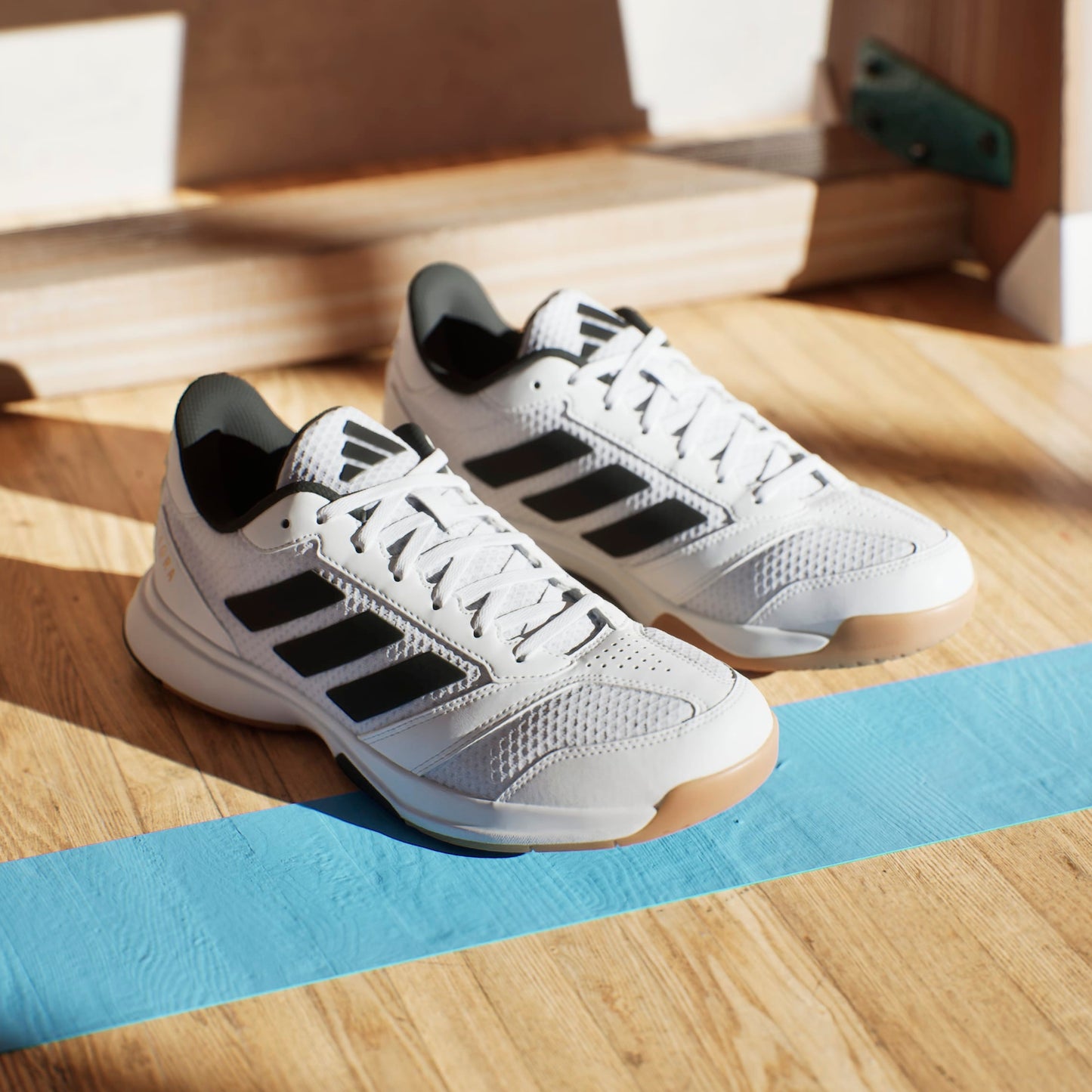 White squash shoes with black stripes on a wooden floor