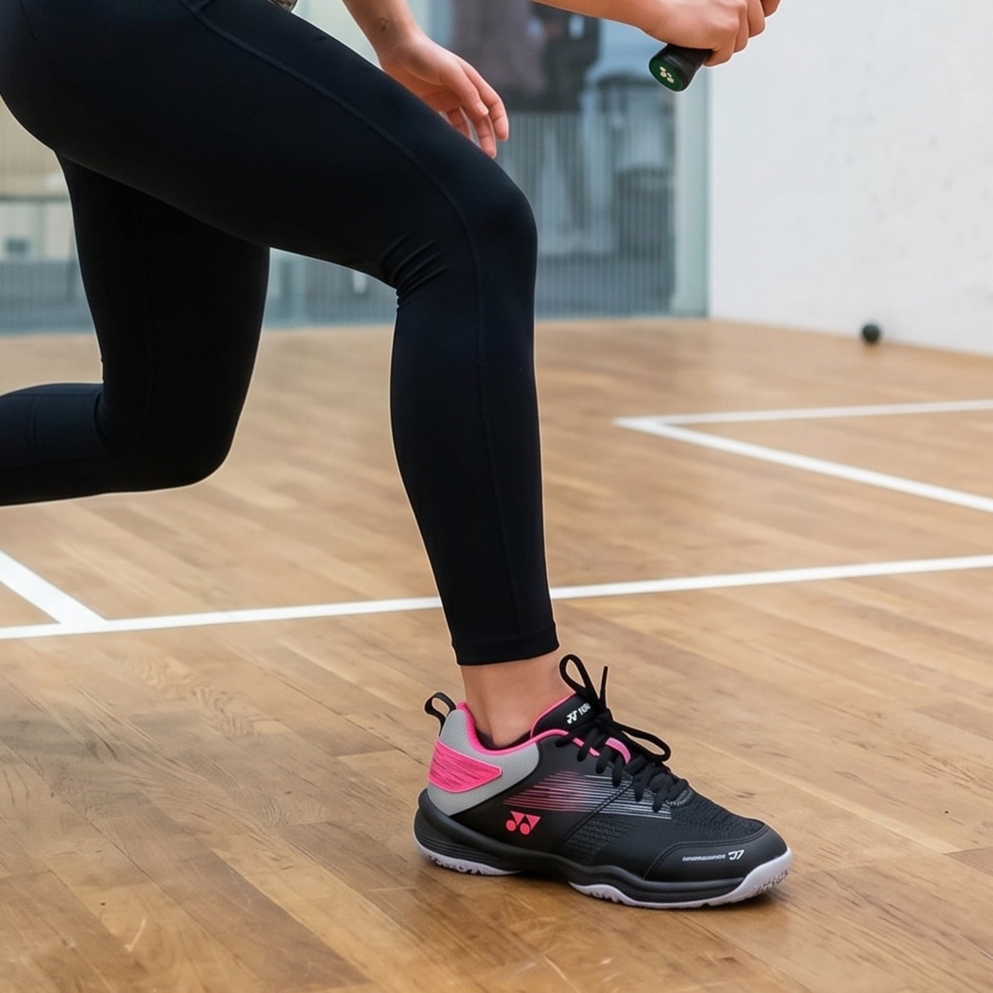 Person wearing black leggings and black and pink athletic shoes on a wooden court.
