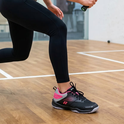 Person wearing black leggings and black and pink athletic shoes on a wooden court.