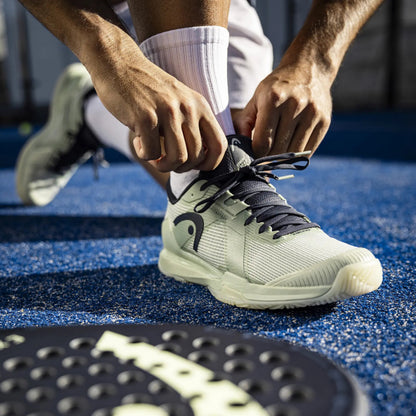 Person tying shoelaces on a sports shoe with a brand logo on a blue surface