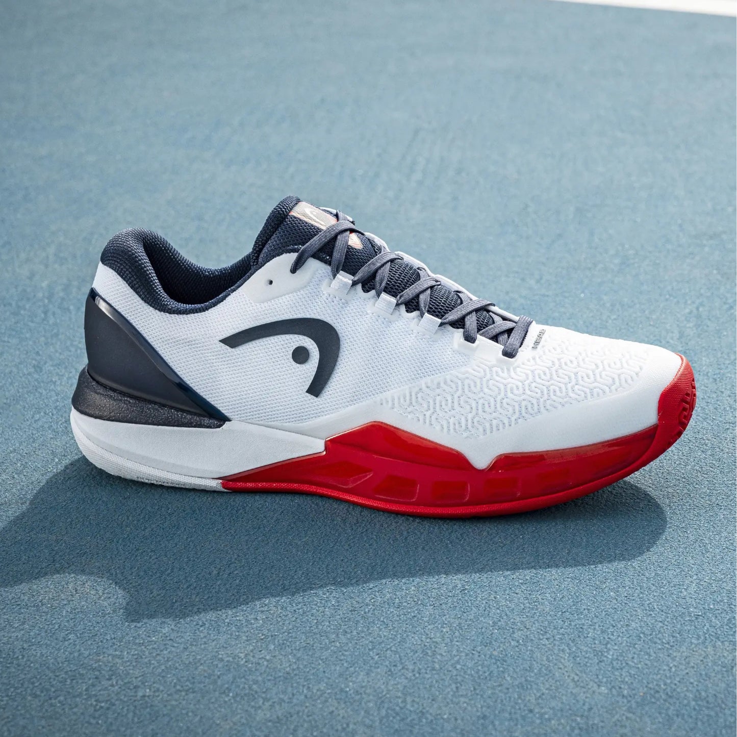 White Head tennis shoe with red sole on a blue court