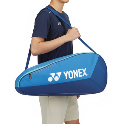 Person holding a blue Yonex tennis racket bag on a white background