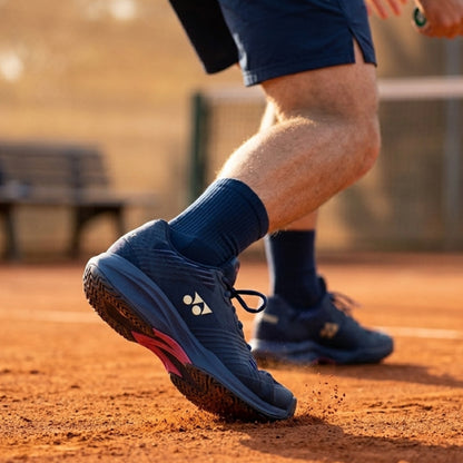 Person wearing blue Yonex tennis shoes on a clay tennis court