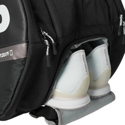 Black tennis bag with a compartment holding white tennis shoes on a white background