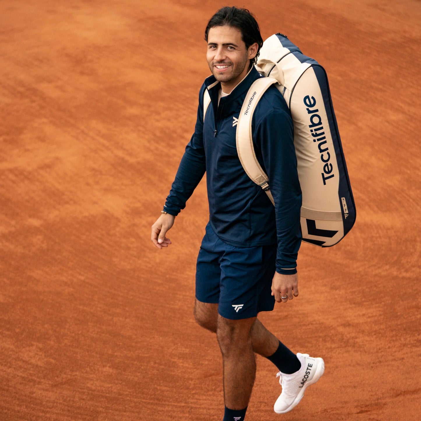 Man walking on a clay tennis court with a Tecnifibre backpack.