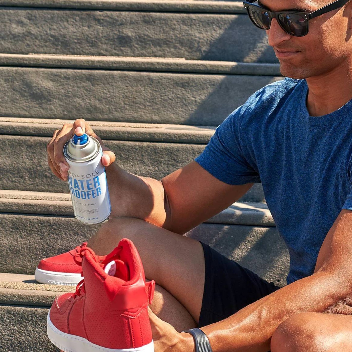 Man sitting on steps holding a can of Sof Sole water proofer spray and a red sneaker.