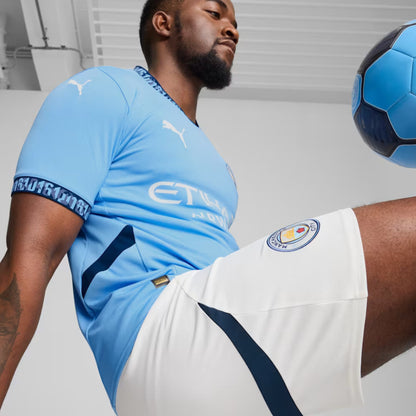 Person wearing a light blue soccer jersey and white shorts with a soccer ball in the background.