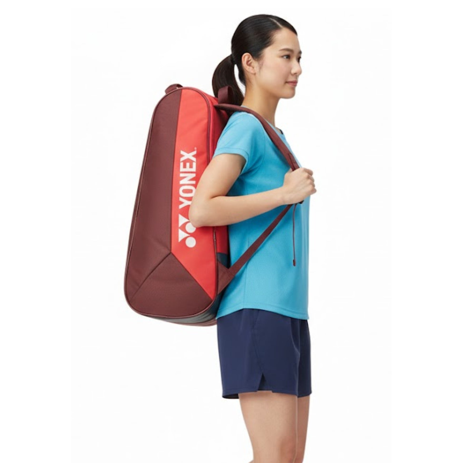 Woman carrying a red and brown Yonex tennis bag on a white background
