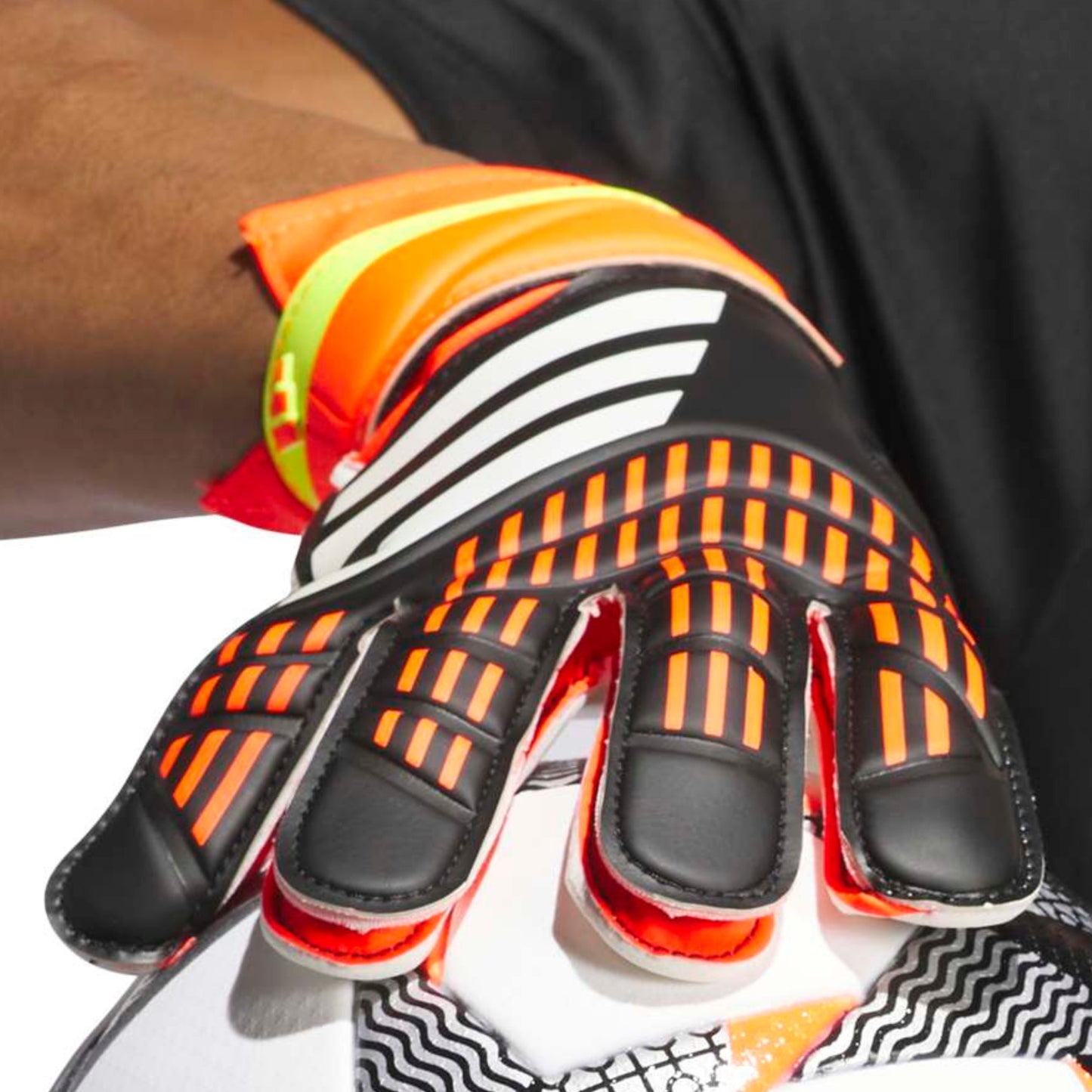 Close-up of a person wearing orange and black soccer goalkeeper gloves on a white background.