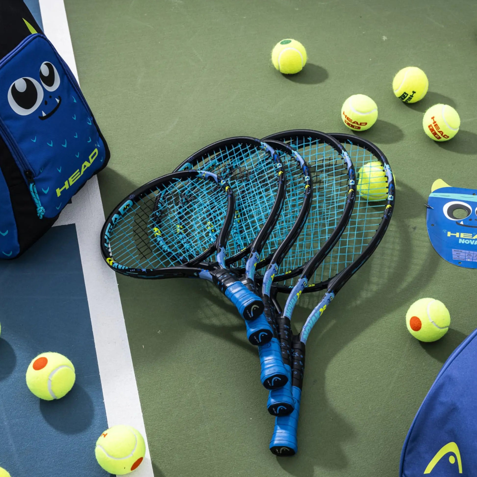 Five tennis rackets with HEAD branding on a green surface surrounded by tennis balls.