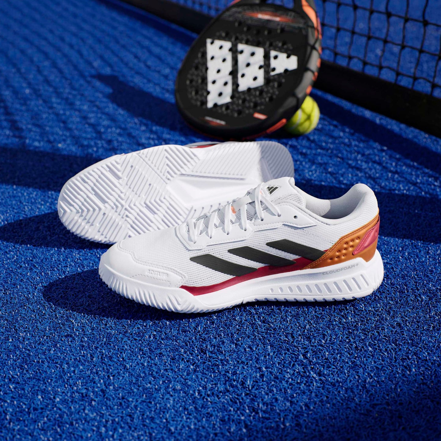 White padel shoes with black and red accents on a blue surface on a sports court.