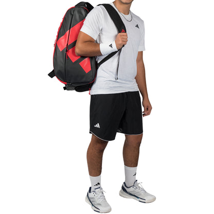 Person wearing a red and black Adidas backpack, white shirt, black shorts, and white sneakers on a white background