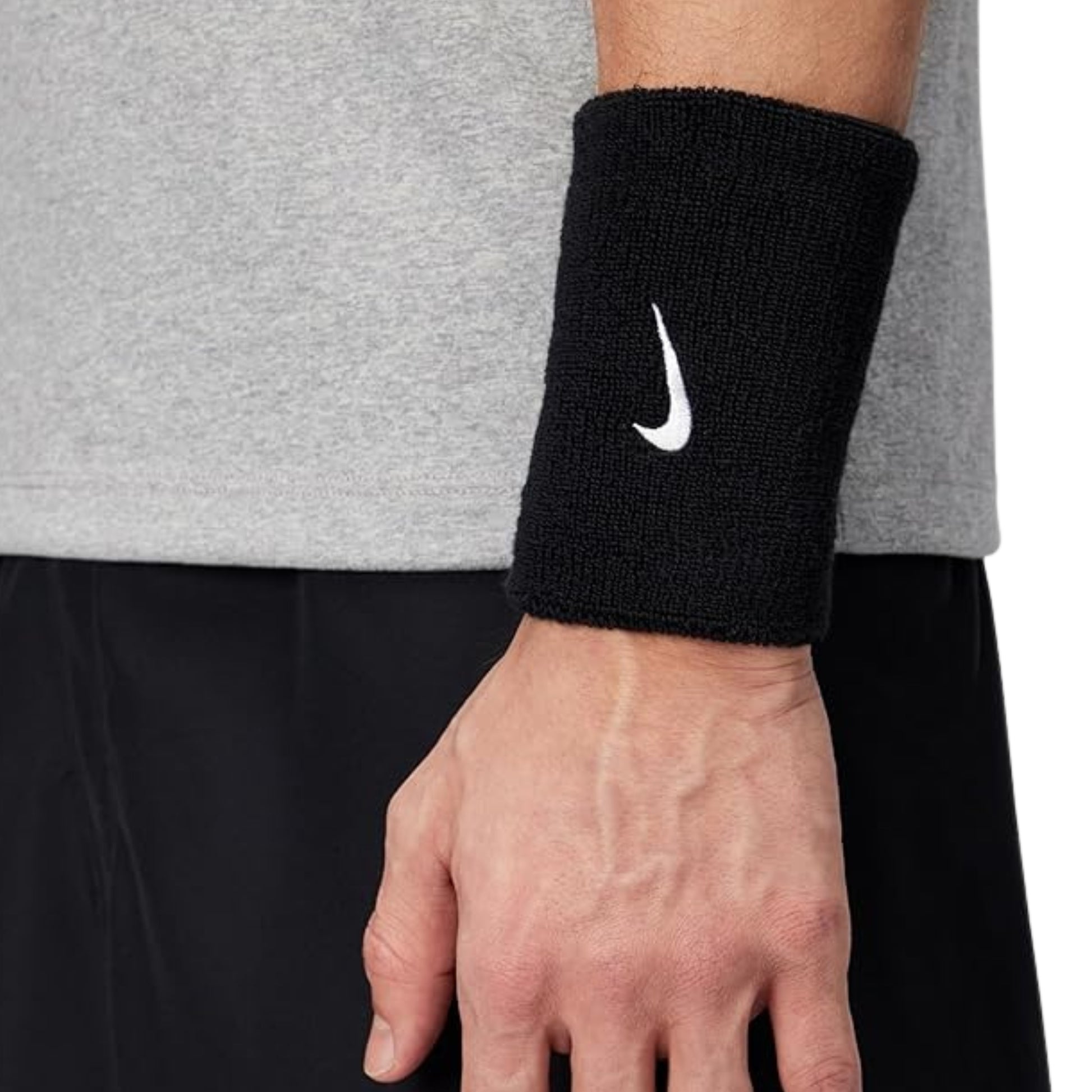 Black wristband with Nike logo on a person's wrist wearing a gray shirt and black pants.
