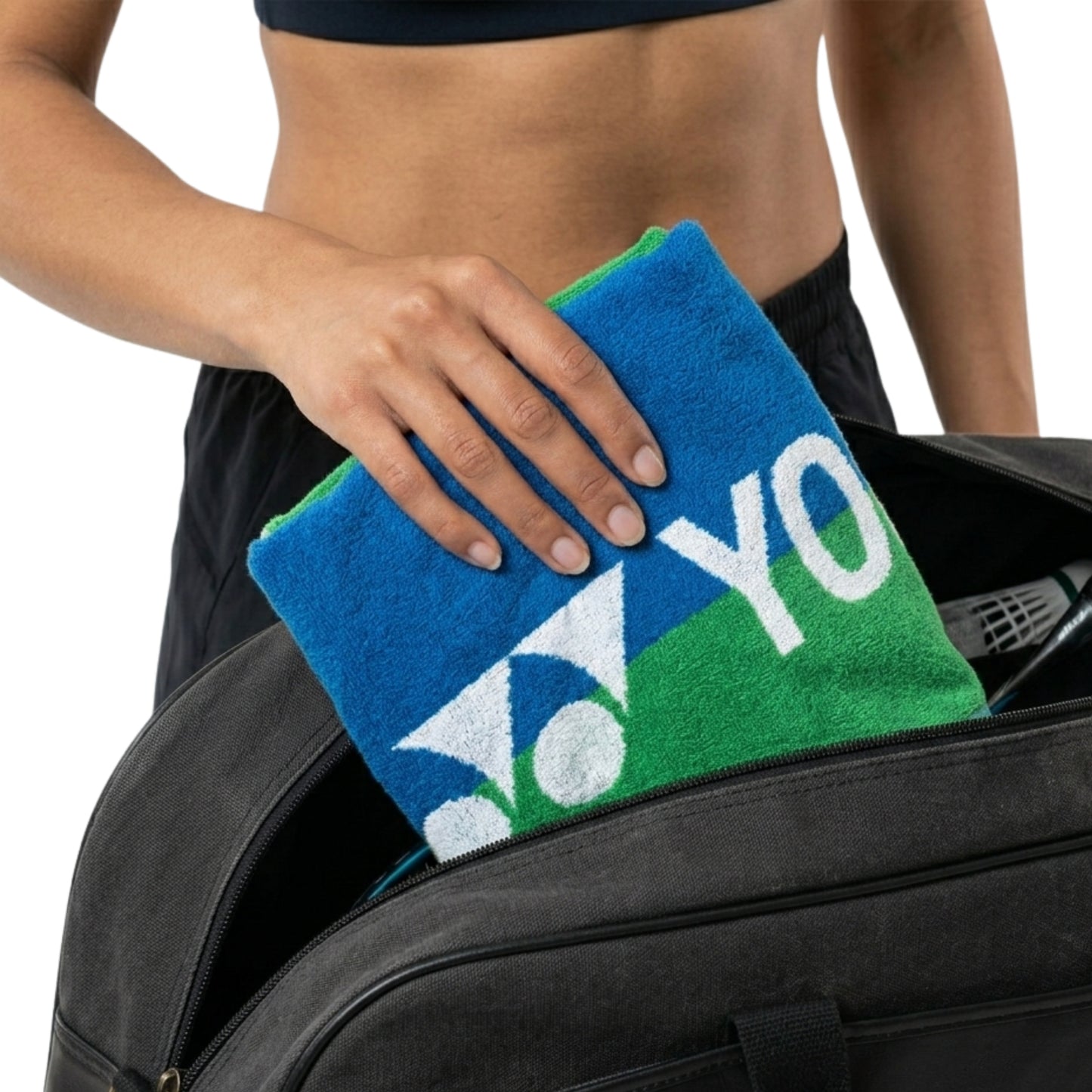 Person holding a blue and green towel with 'YONEX' text, standing next to a suitcase.
