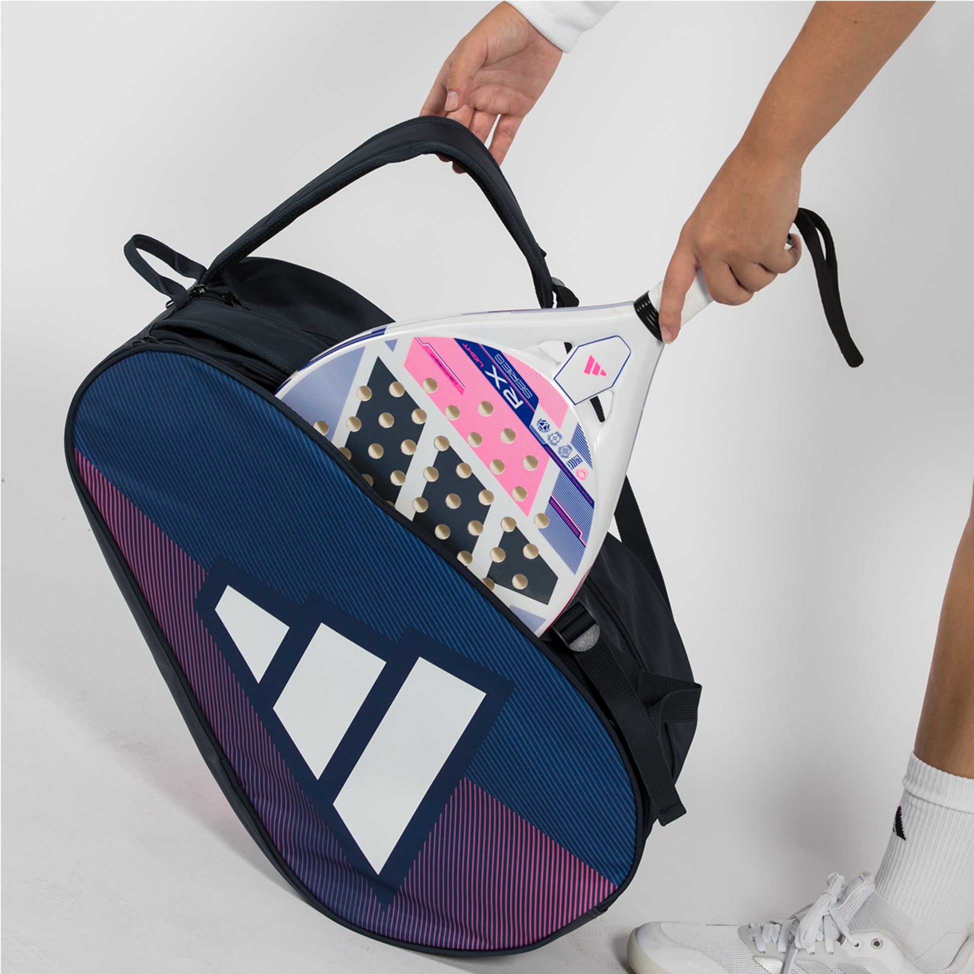 Person holding a blue Adidas racket bag with tennis rackets inside on a white background