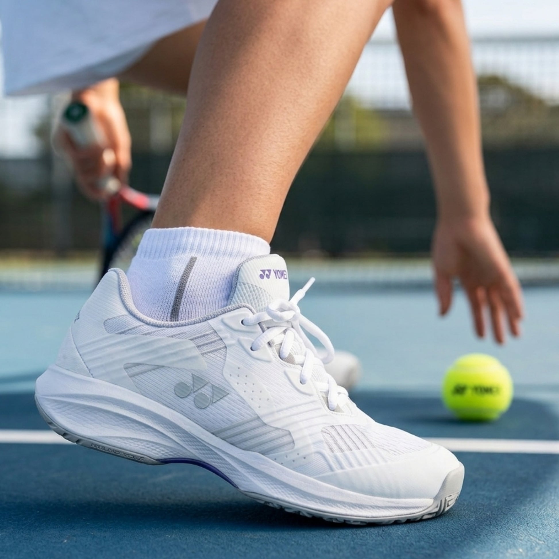 White Yonex tennis shoe with Yonex logo on a tennis court