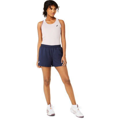 Woman wearing a light rose Asics tank top and navy shorts on a white background