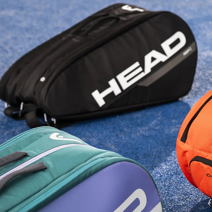 Black HEAD tennis bag, green and blue sports bag, and orange basketball on a blue surface.