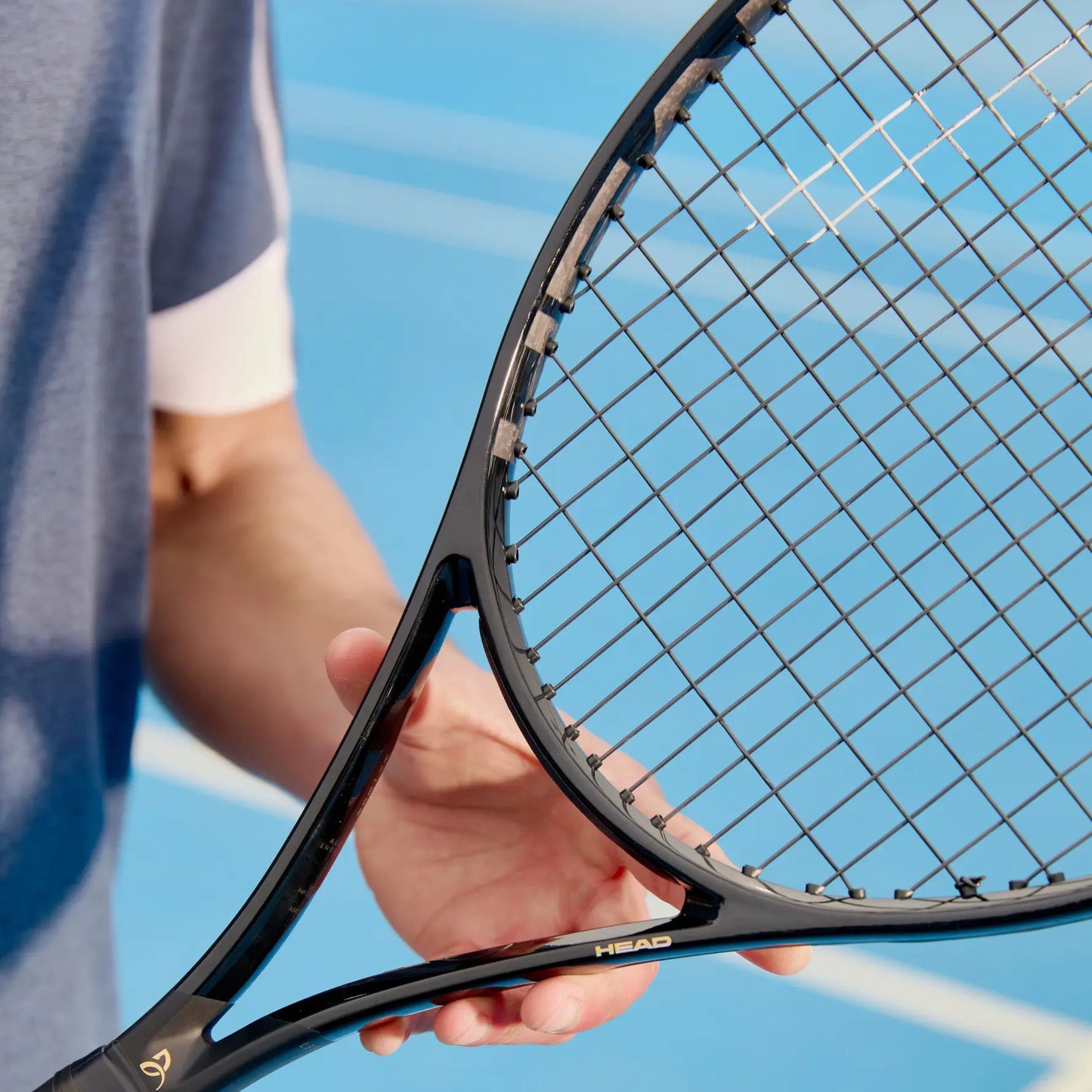 Close-up of a black Head tennis racket held by a person on a tennis court