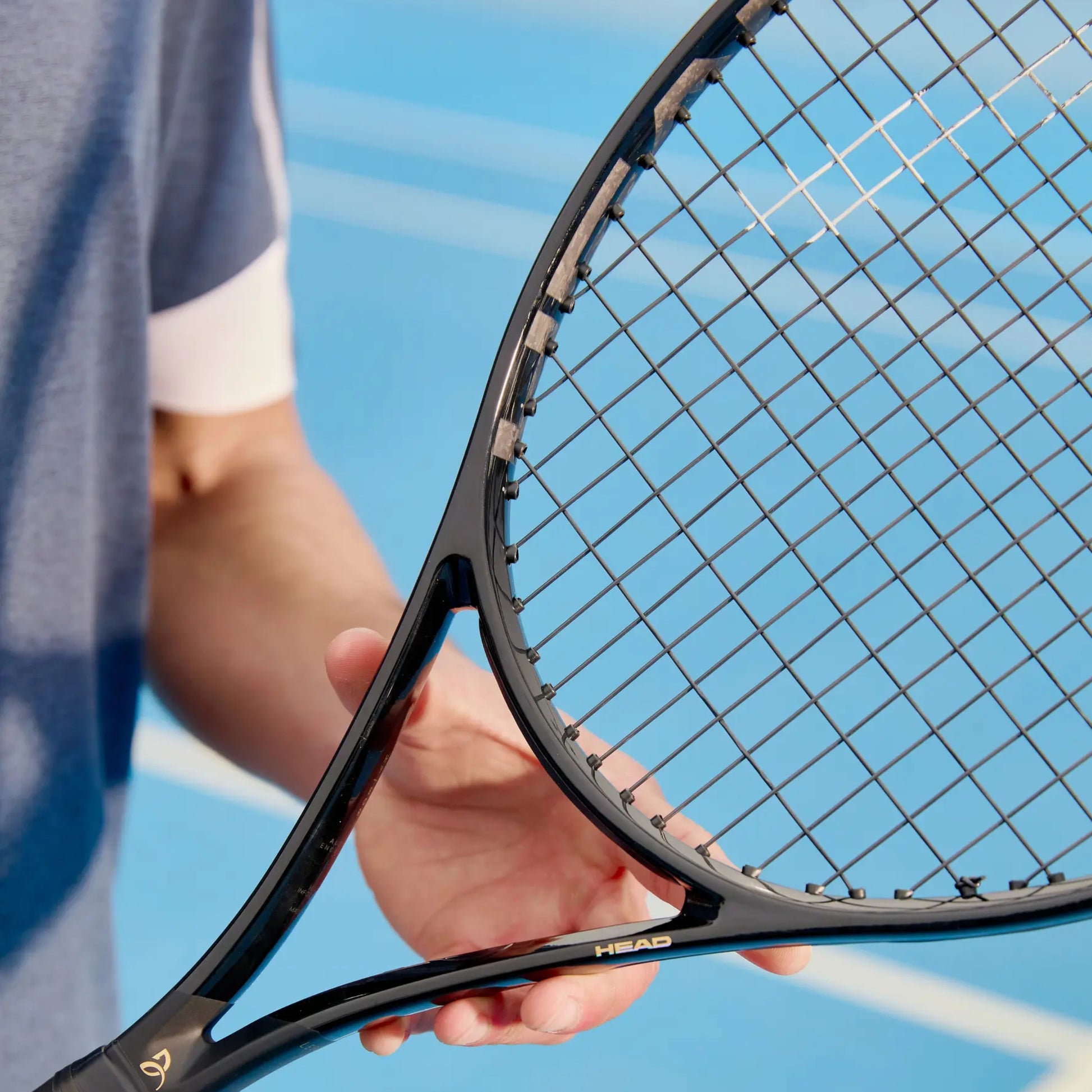 Close-up of a black Head tennis racket held by a person on a tennis court