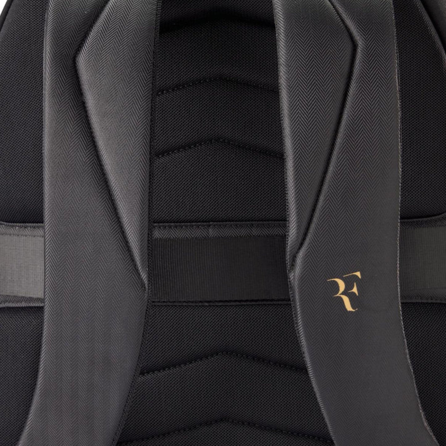 Close-up of a black backpack with a gold logo on the strap.