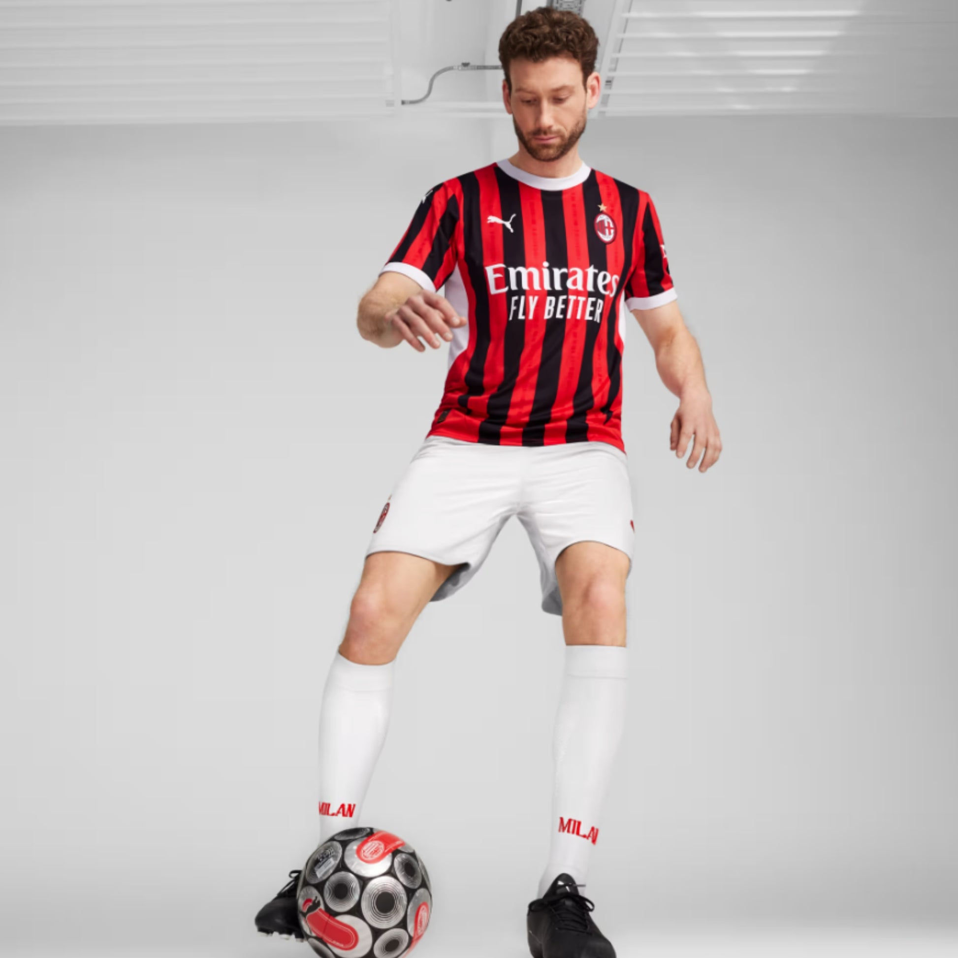 Person wearing a red and black soccer jersey with white shorts, standing on a gray background.