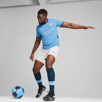 Person wearing a light blue Puma soccer jersey with white shorts, dark blue socks, and black cleats, posing with a soccer ball on a plain background.