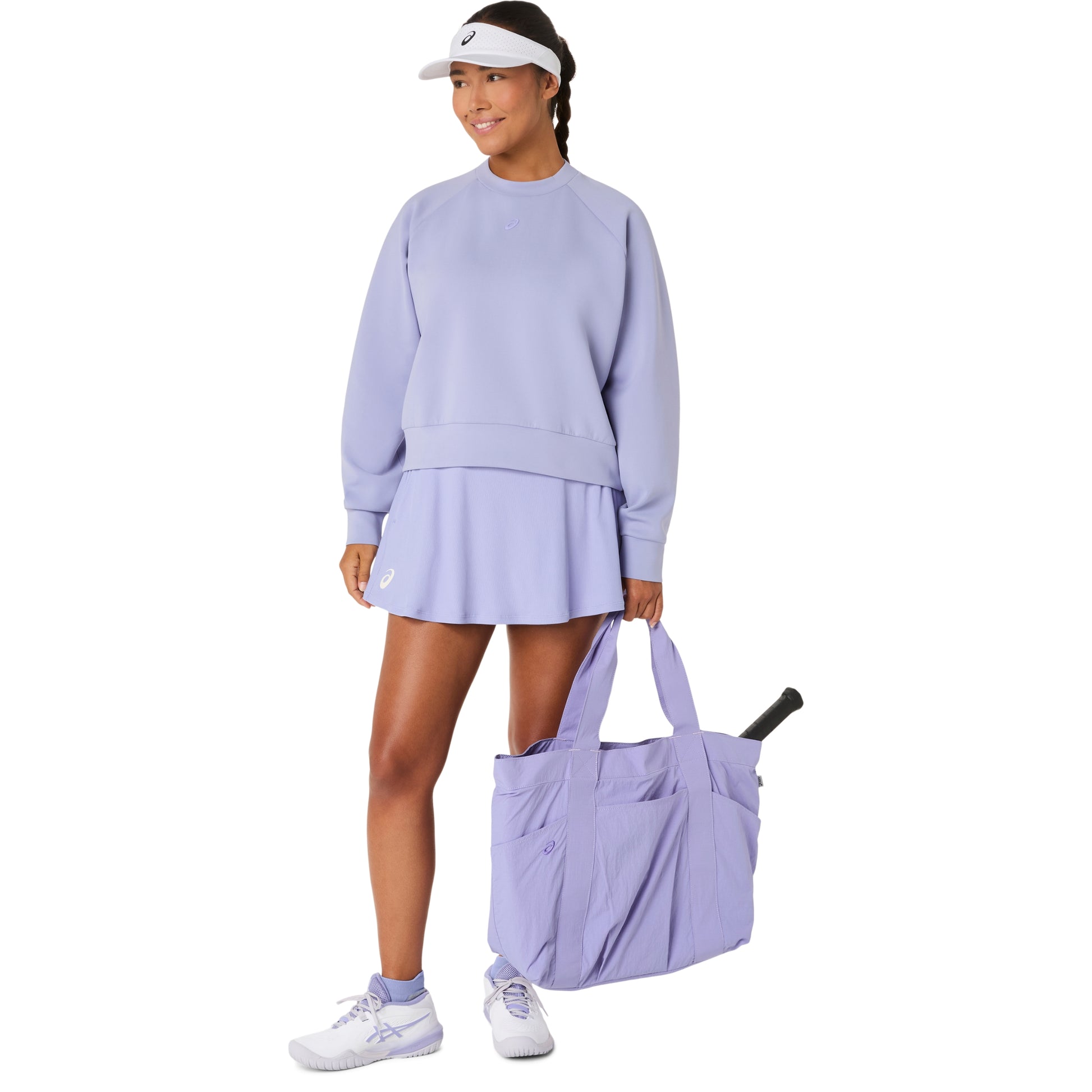 Woman in lavender tennis outfit holding a matching bag on a white background