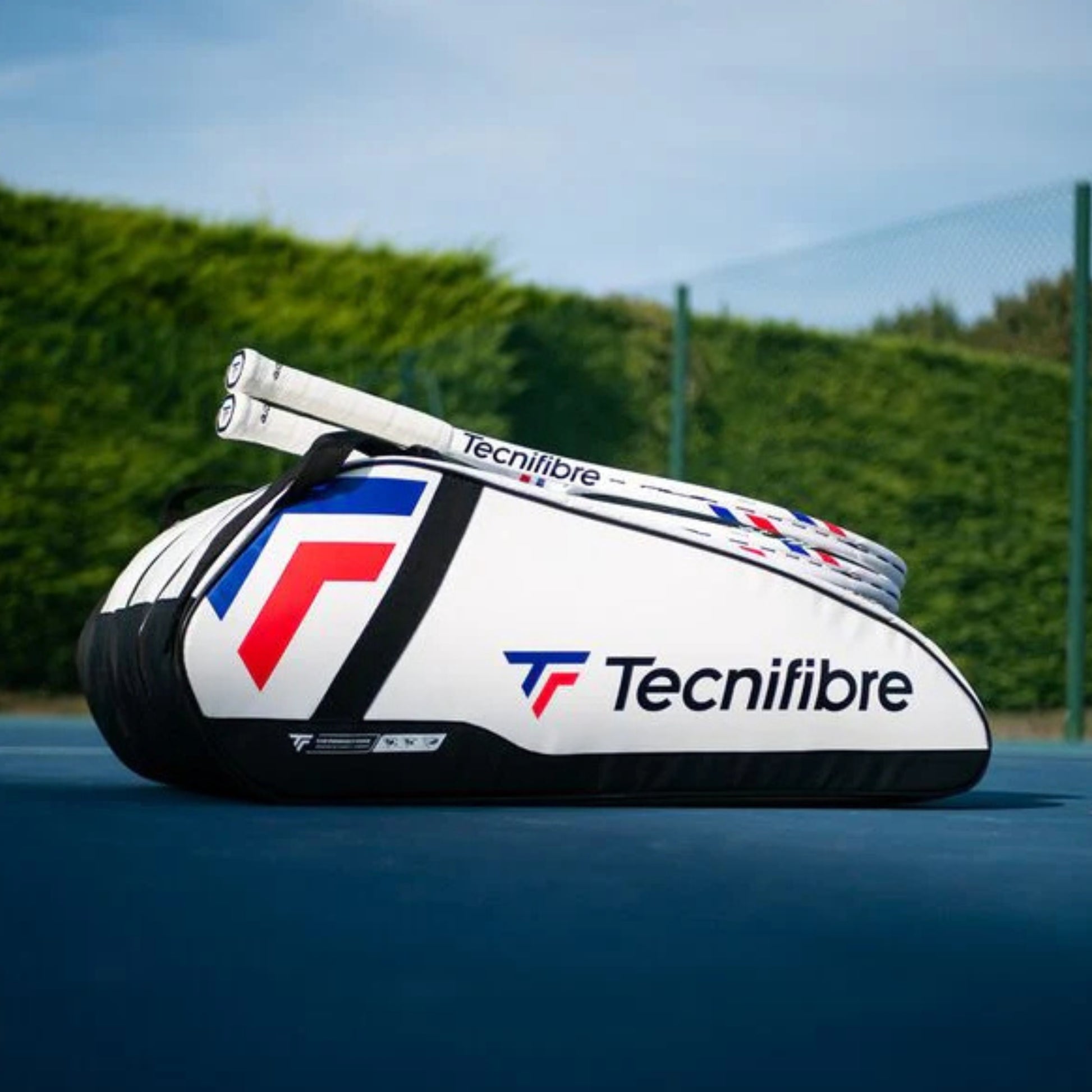 Tecnifibre tennis racket bag on a tennis court with a clear blue sky.